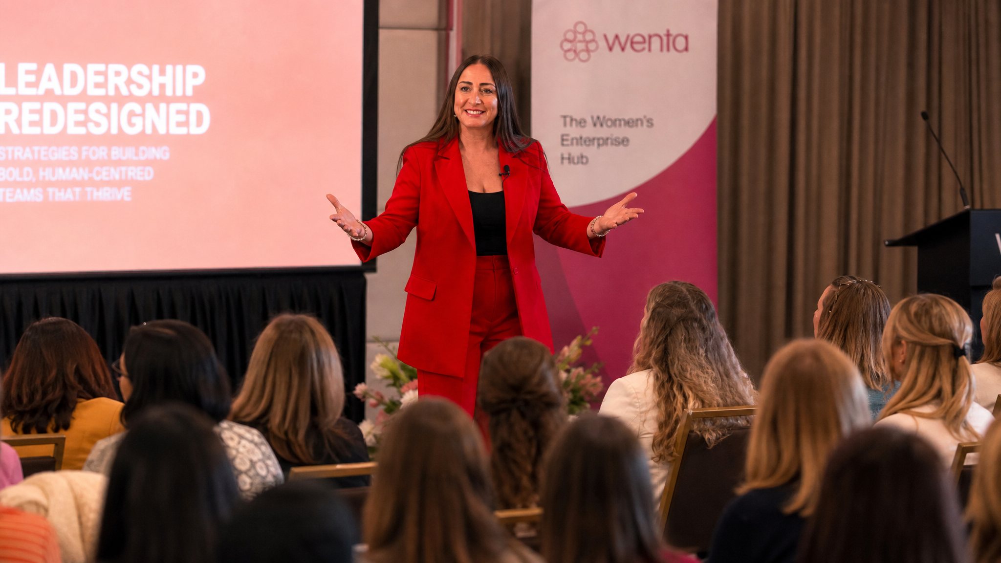Michelle Louise Crook on stage with a microphone, speaking to a seated audience
